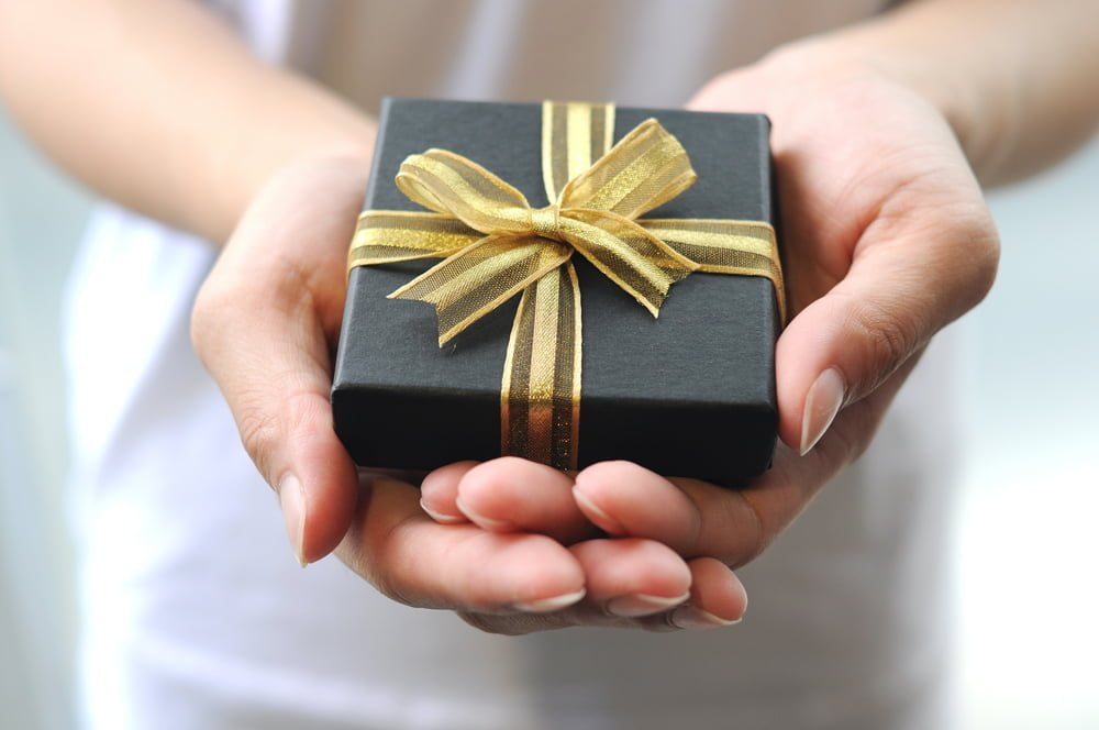 Closeup of hands holding a black gift package with a golden band