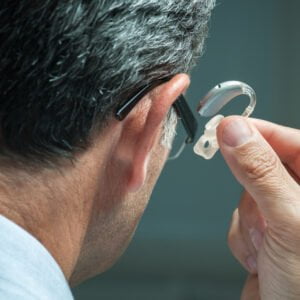 Senior man having just taken off/ about to insert hearing aid in his right ear