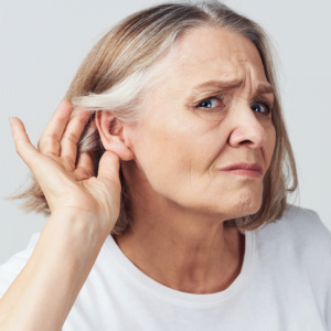 Senior woman looking at camera, holding her hand to her ear, visibly struggling to hear.