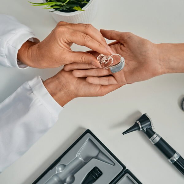 Audiologist placing an advanced hearing aid model in the hand of a patient.