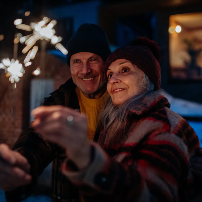 A senior couple enjoying sparklers outdoors while wearing hearing protection